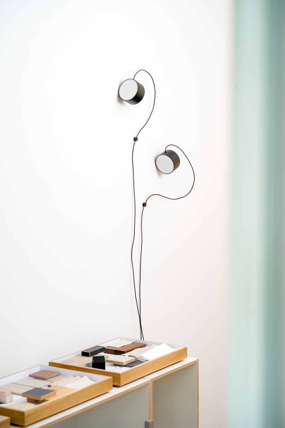 Materialbibliothek im Architekturbüro mit ausgewählten Holz-, Stein-, Keramik- und Stoffmustern auf einem Sideboard. Filigrane Wandleuchten unterstreichen die ruhige Arbeitsatmosphäre.