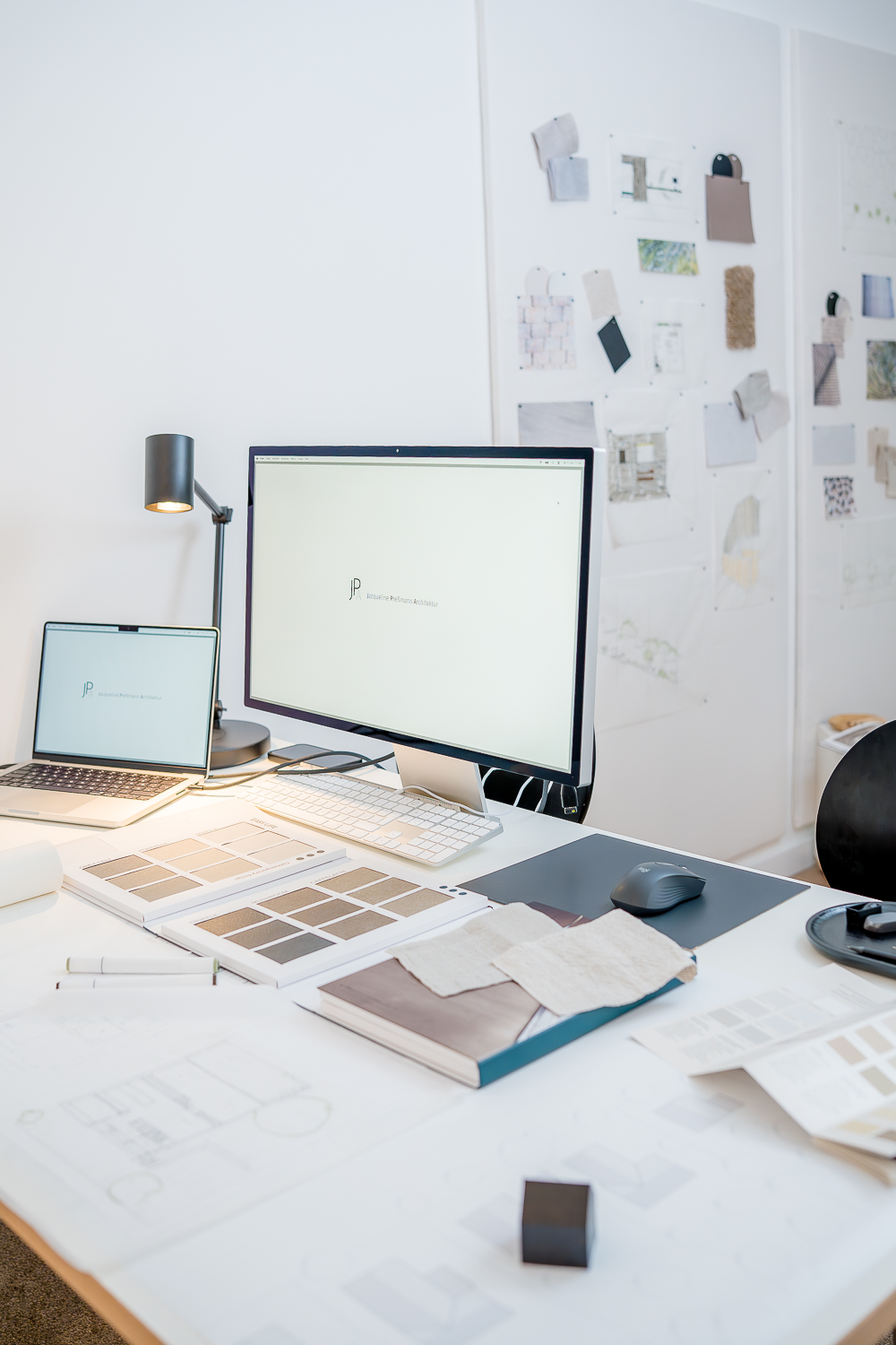 Arbeitsplatz im Architekturbüro mit Computer, Skizzen, Materialmustern und Moodboards. Digitale Planung und analoge Materialauswahl ergänzen sich im kreativen Entwurfsprozess.