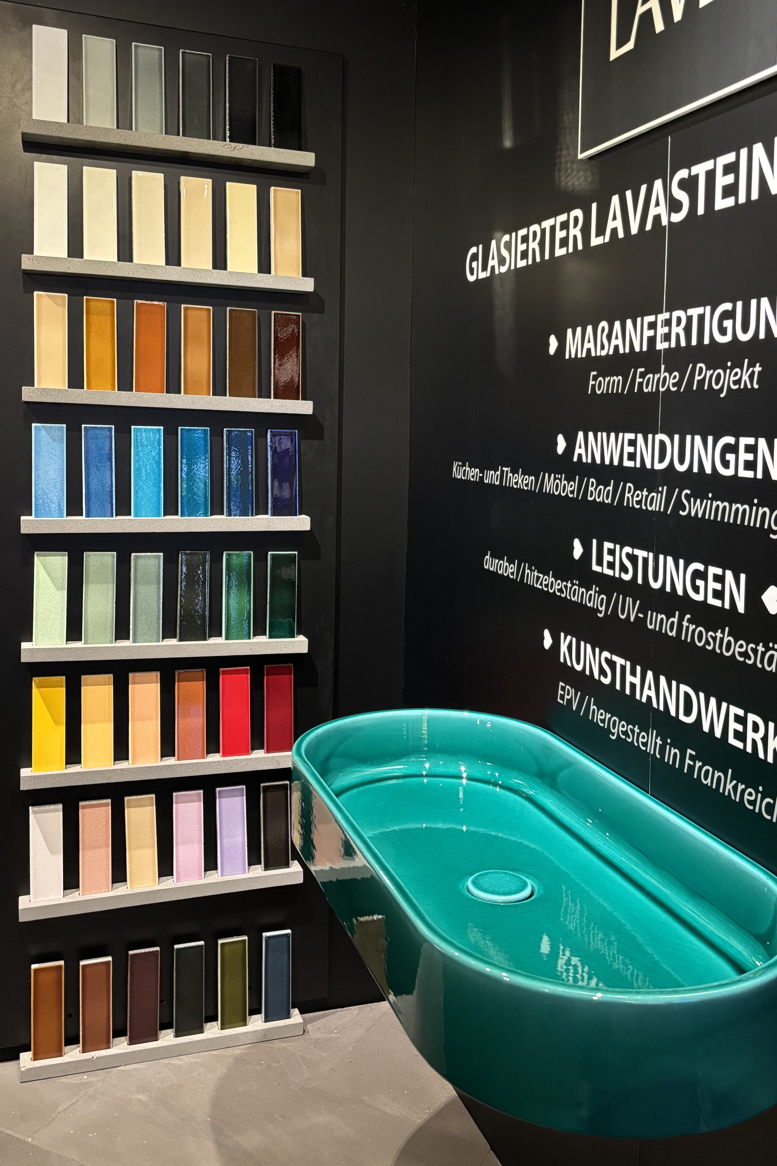 JPA_Aktuelles_architectatwork_4 Messestand mit glasiertem Lavastein: Farbige Materialmuster von hellen Naturtönen bis zu kräftigen Blau-, Grün- und Rottönen sowie ein türkisfarbenes Waschbecken aus glasiertem Lavastein