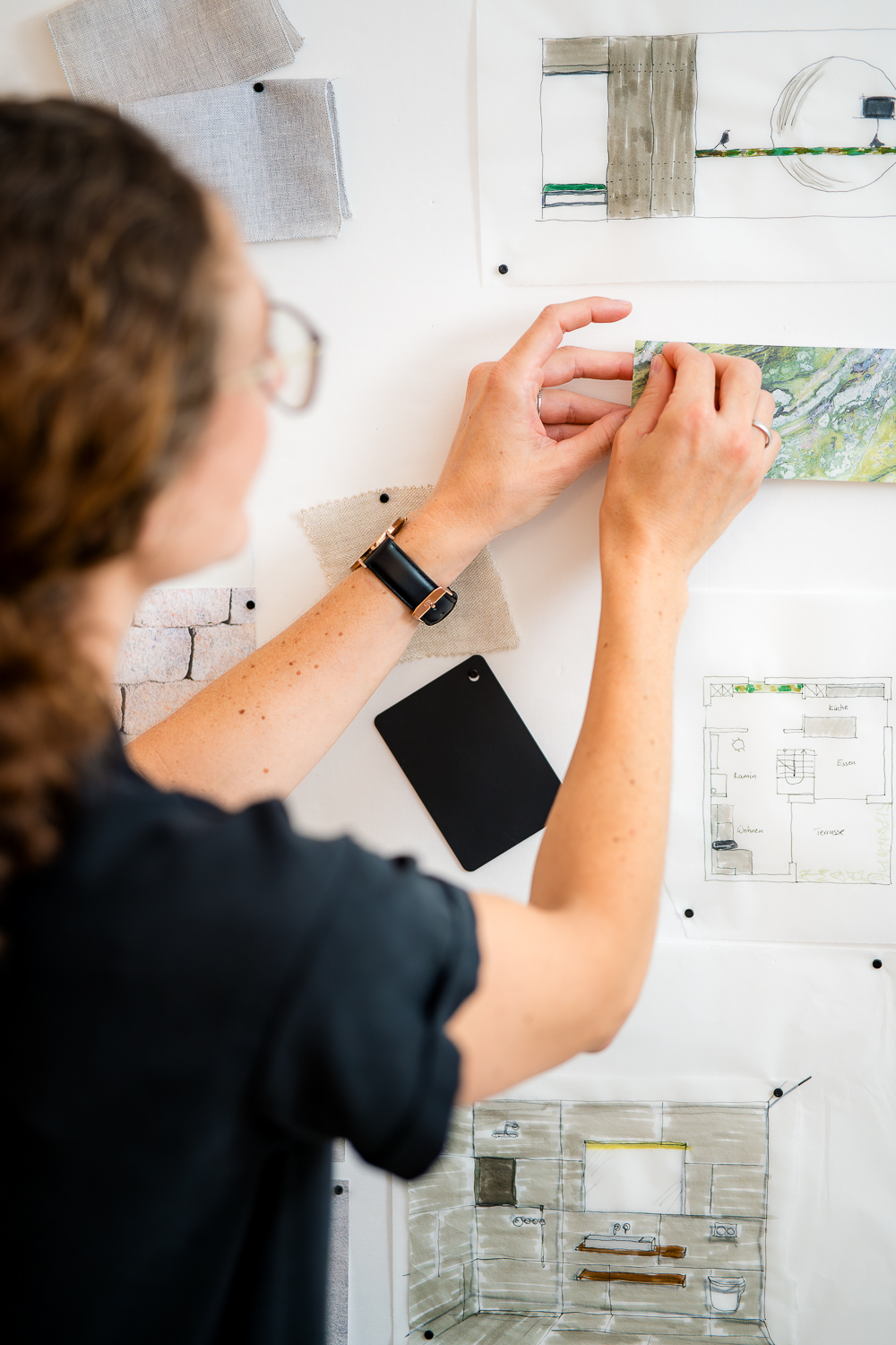 Detailbild Hände der Architektin Jacqueline Preßmann beim Zusammenstellen von Materialmustern und Entwurfsskizzen an einer Pinnwand