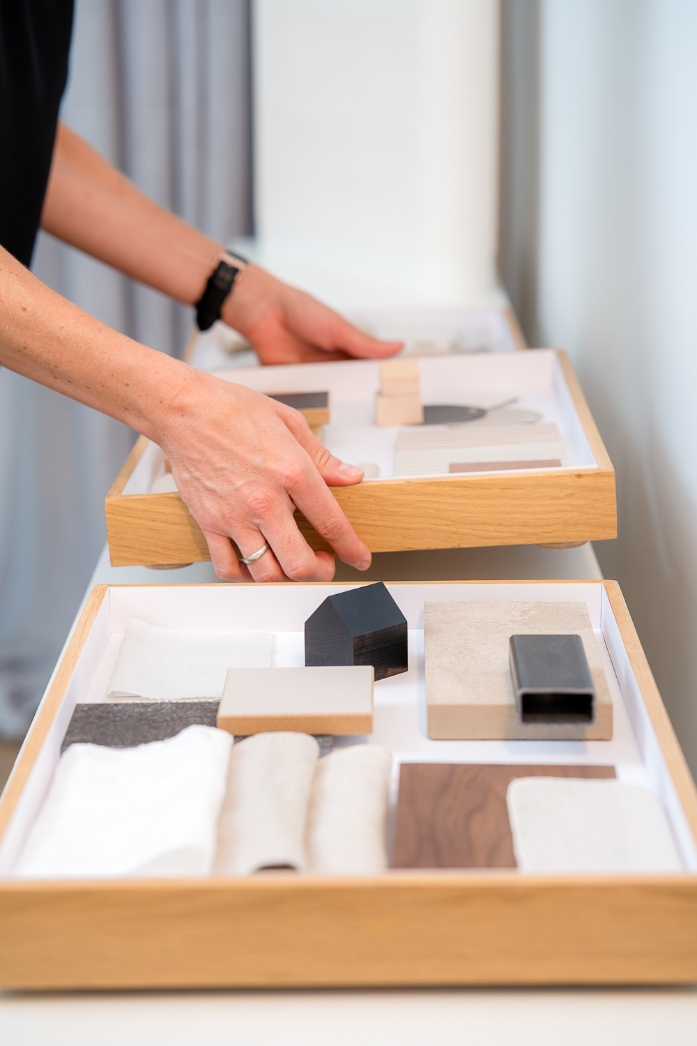 Detailbild Hände der Architektin Jacqueline Preßmann beim Zusammenstellen von Materialmustern für ein Architekturkonzept auf Materialtabletts aus Eichenholz