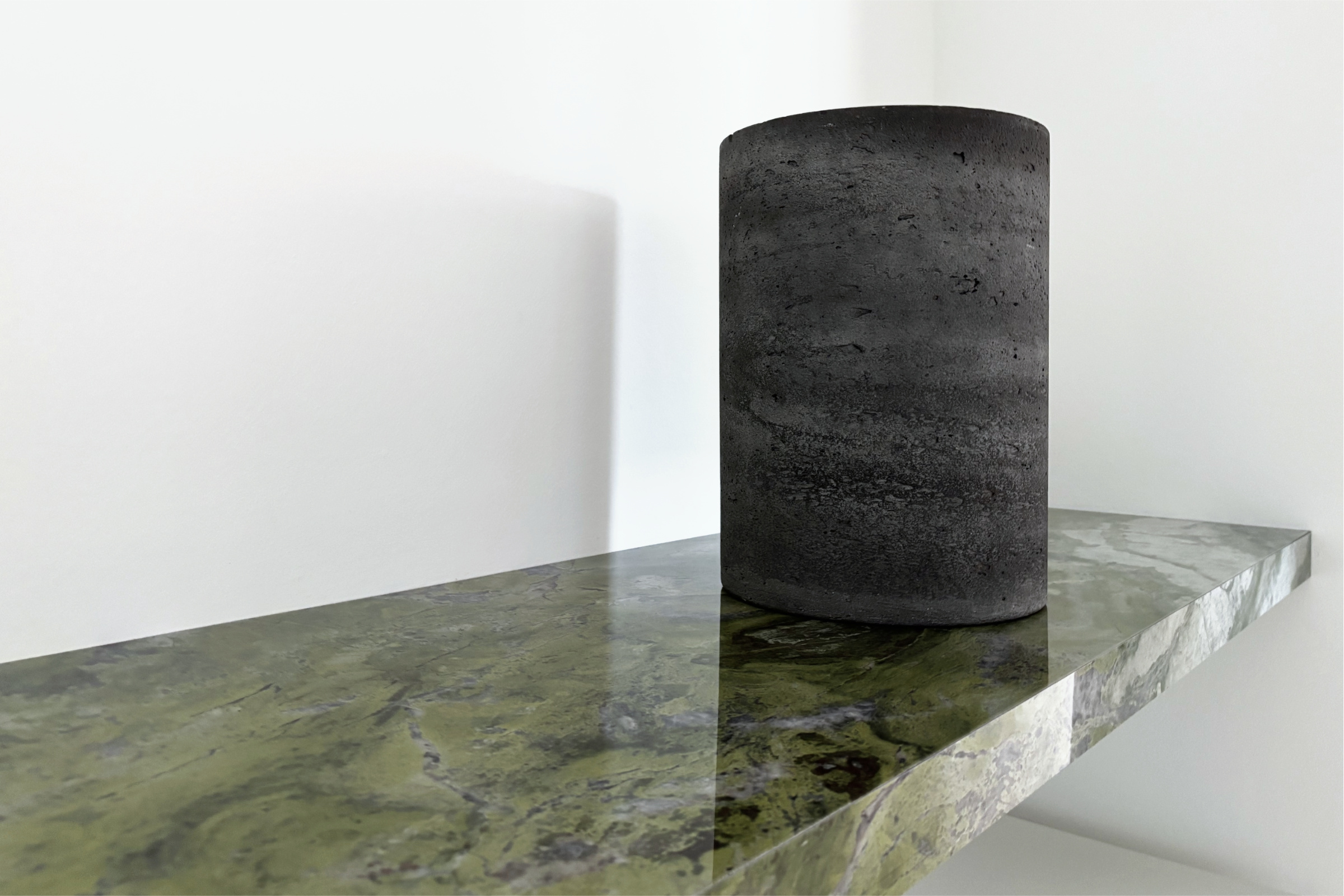 Detailaufnahme des drei Meter langen Green-Marble-Boards im Eingangsbereich. Großformatige Platte aus einem Stück, darauf zylindrische Betonvase, natürliches Licht erzeugt Schattenwurf an der Wand und Spiegelung auf der polierten Oberfläche